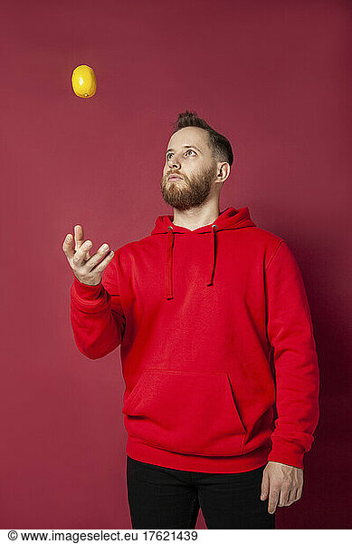 Man playing with lemon against red background