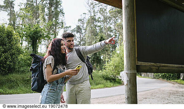 Man pointing by girlfriend holding smart phone standing at roadside