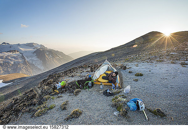 Man pokes head out of tent at sunset while camping on mountain ridge.