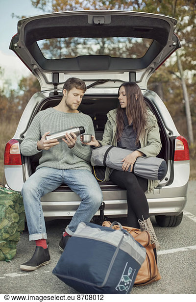 Man pouring coffee for woman while sitting at car trunk during camping