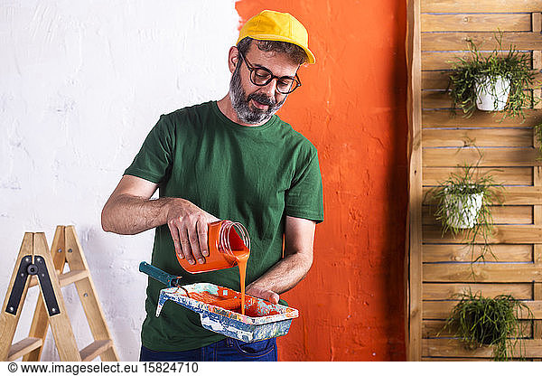 Man pouring orange paint into paint tray