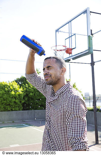 Man pouring water on head while standing in basketball court