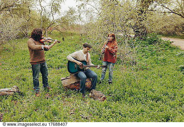 Man practicing guitar with friends playing violin and clarinet in field