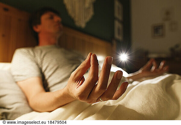 Man practicing Lotus position on bed at home
