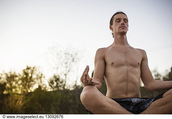 Man practicing yoga in lotus position against clear sky