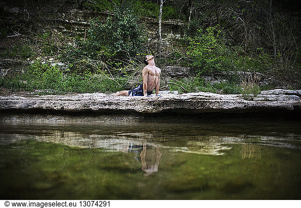 Man practicing yoga in upward facing dog pose by lake