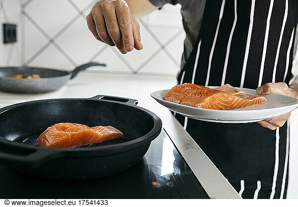 Man preparing fish in cooking pan at home