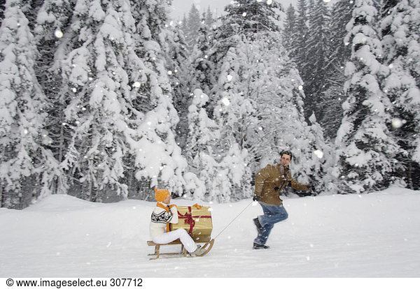 Man pulling woman holding present on sledge  side view