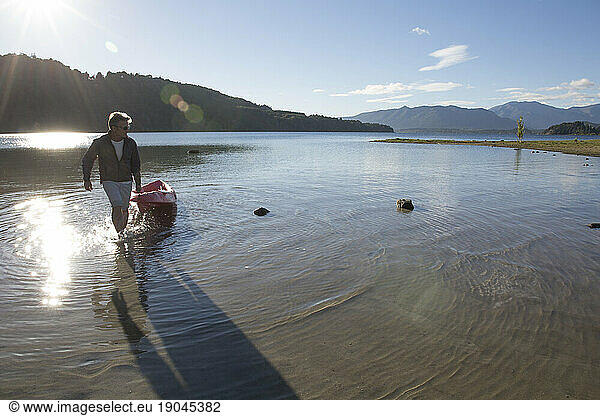 Man pulls kayak ashore from mountain lake at sunrise