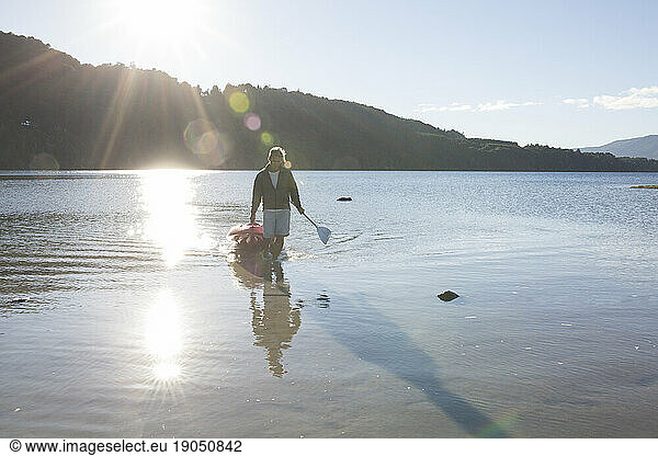 Man pulls kayak ashore from mountain lake at sunrise