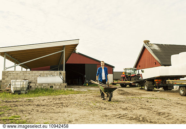 Man pushing wheelbarrow on dirt road by tractor against barn at farm