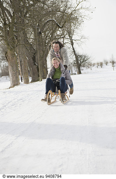 Man pushing woman on sledge in snow