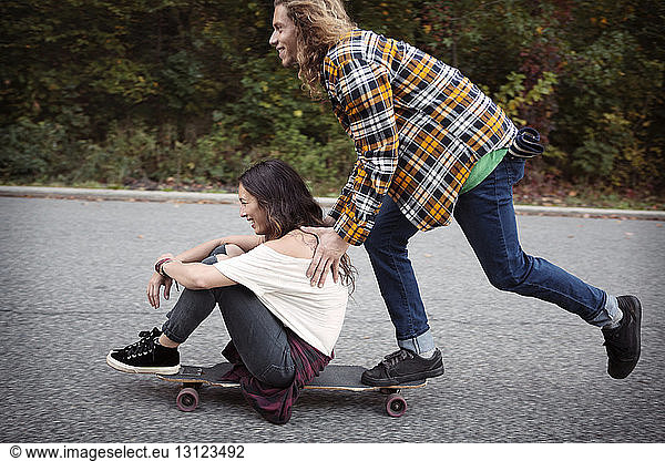 Man pushing woman sitting on skateboard at street