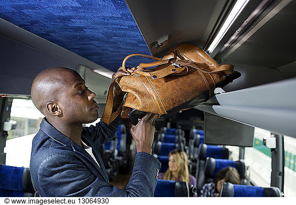 Man putting bag in luggage rack in bus