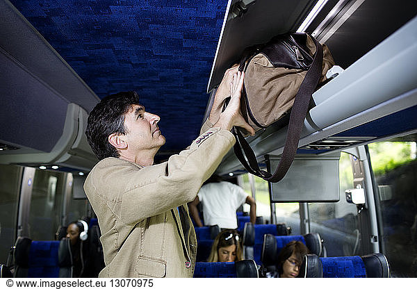 Man putting bag in luggage rack while standing in bus