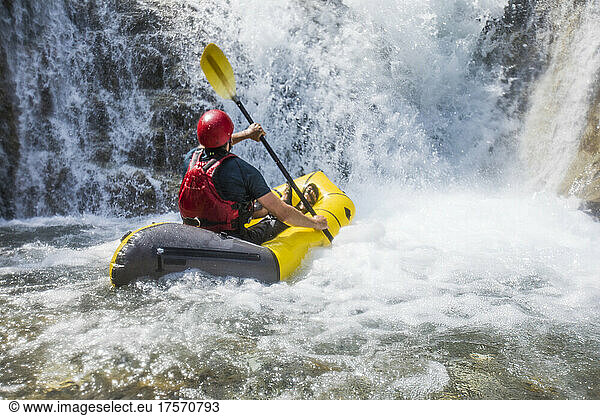 Man rafting on river below large waterfall in British Columbia Canada.
