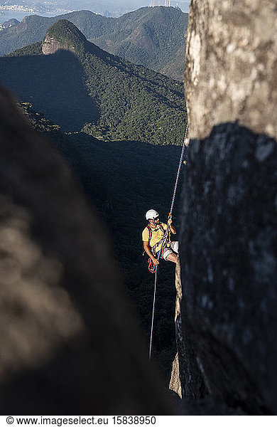 Man rappelling steep rocky mountain with beautiful view to rainforest
