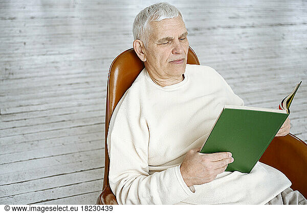 Man reading book sitting on chair at home