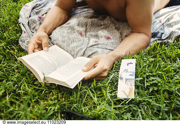 Man reading book while relaxing on grassy field