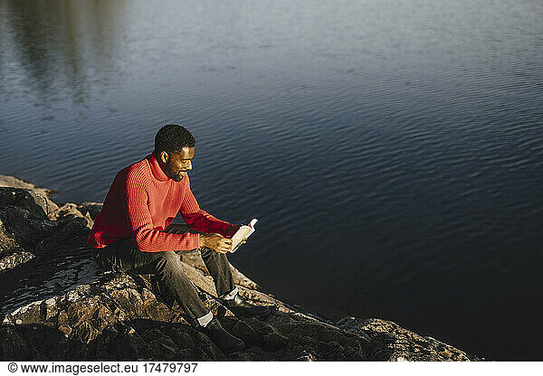 Man reading book while sitting on rock during weekend