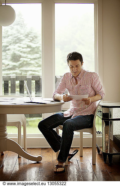 Man reading document while sitting on chair by table at home