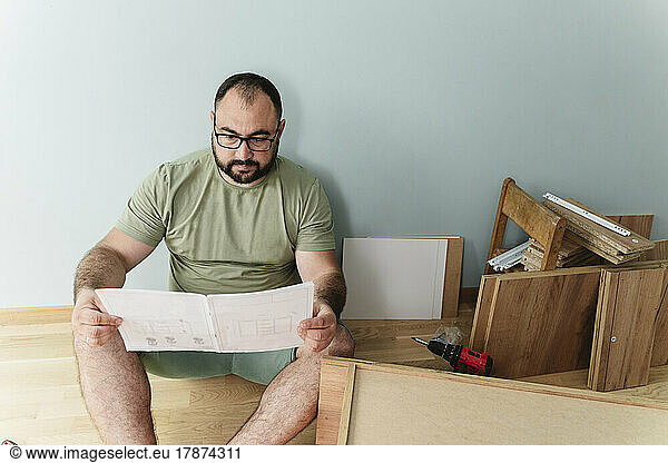 Man reading instruction manual sitting on floor at home