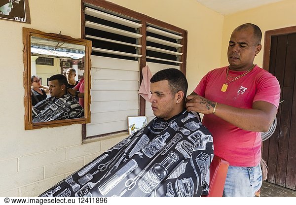 Man receiving hair cut from an outdoor barber in Nueva Gerona on Isla de la Juventud  Cuba.