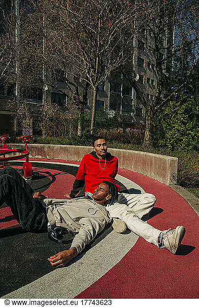 Man relaxing on male friend's lap in playground on sunny day