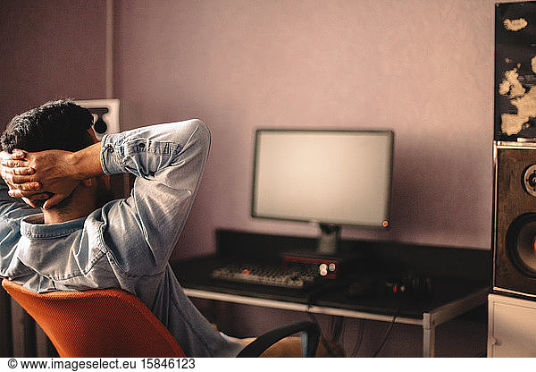 Man relaxing sitting on chair by computer with hands behind head
