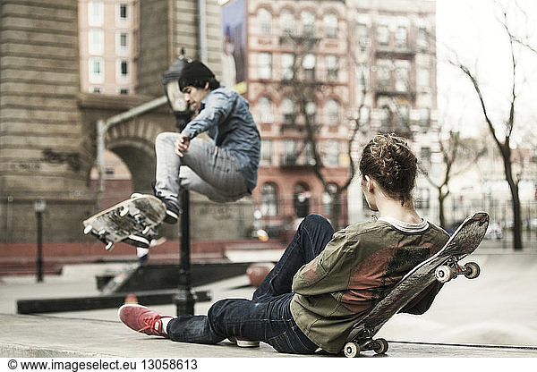 Man relaxing while friend skateboarding at skateboard park