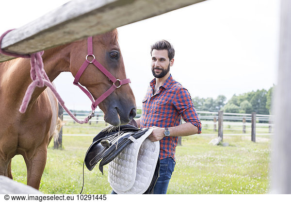 Man removing saddle from horse in rural pasture