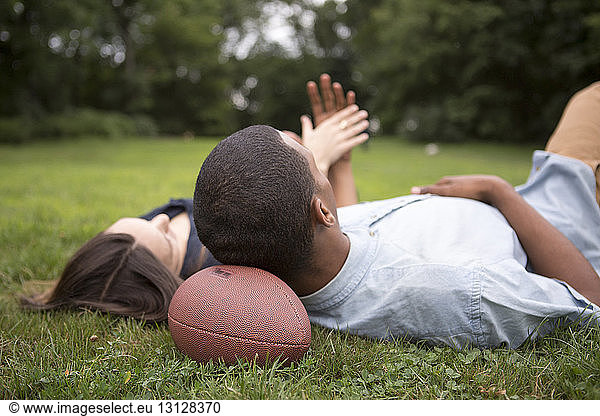 Man resting head on football ball while lying with woman on field