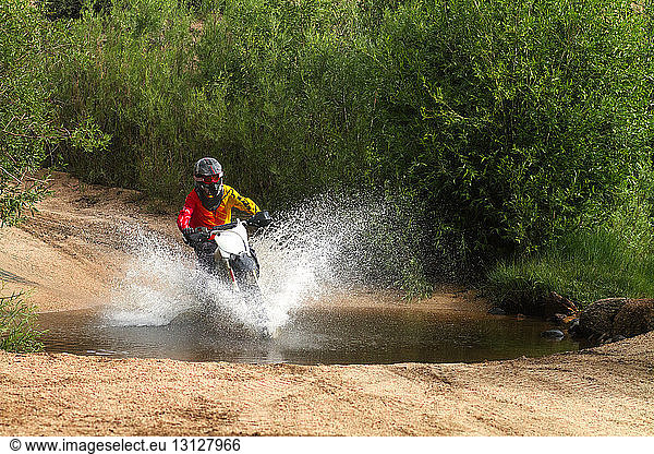 Man riding dirt bike and splashing water in puddle