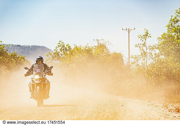 Man riding his adventure motorbike on dusty road in Cambodia