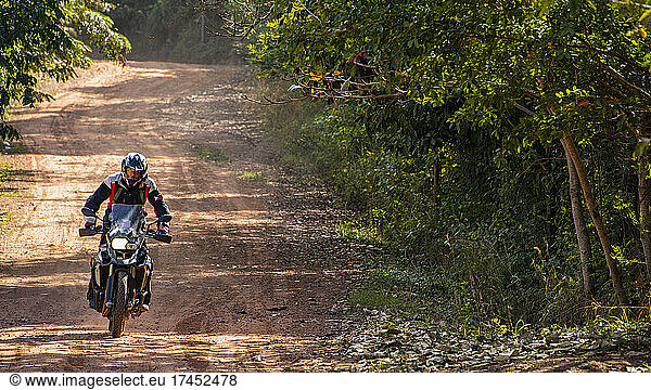 Man riding his adventure motorbike on dusty road in Cambodia