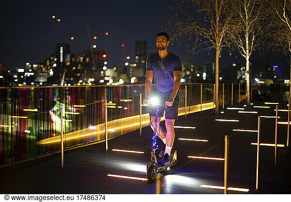 Man riding illuminated scooter in city at night  London  UK