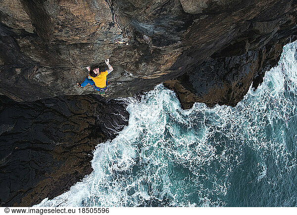 Man rock climbing on seaside cliff with waves crashing below