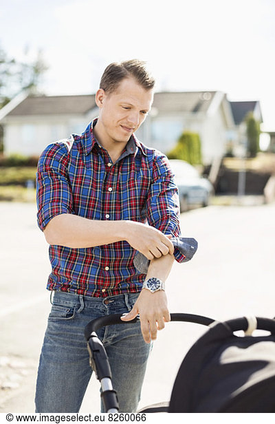Man rolling up shirt sleeve while looking at baby carriage on street