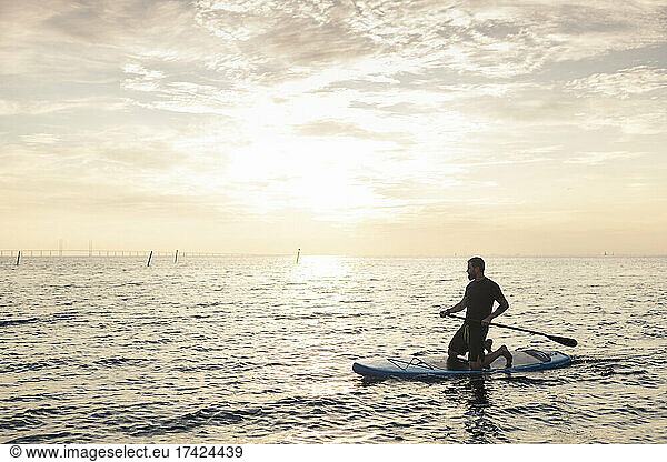 Man rowing paddleboard in sea during sunset