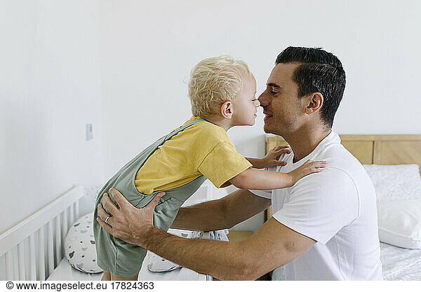 Man rubbing nose with son on bed at home