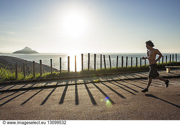 Man running on street by sea against sky during sunny day