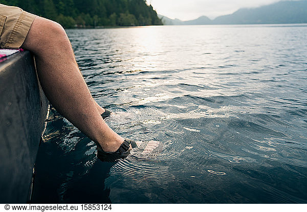 Man's feet in sandals dipped into lake