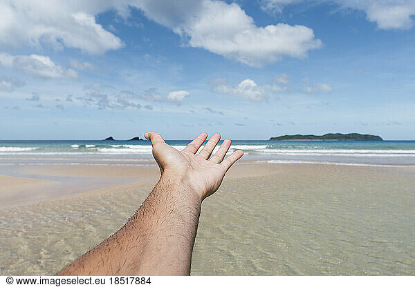 Man's hand reaching towards sea at beach
