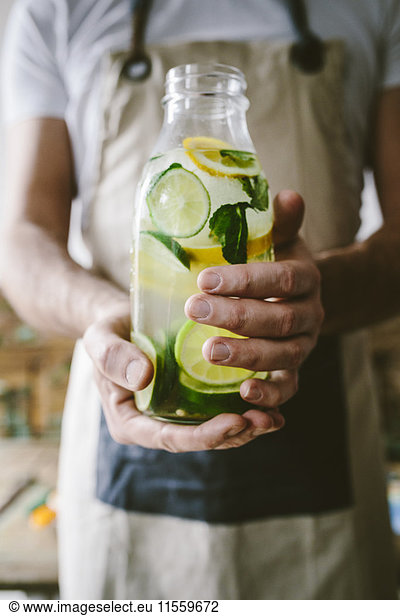 Man's hands holding glass bottle of infused water with lemon  lime  mint leaves and ice cubes