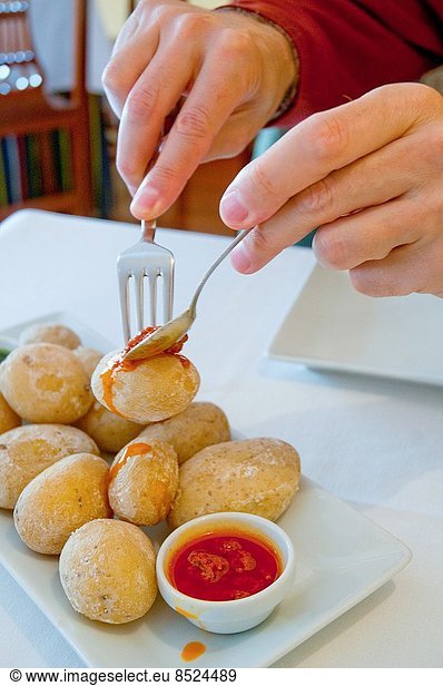Man´s hands serving himself papas arrugadas with red mojo sauce in a Canarian restaurant. Canary Islands  Spain.