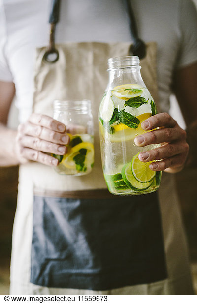 Man's handsholding glass bottle of infused water with lemon  lime  mint leaves and ice cubes