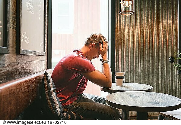 man sat feeling stressed with his face in his hands in a cafe