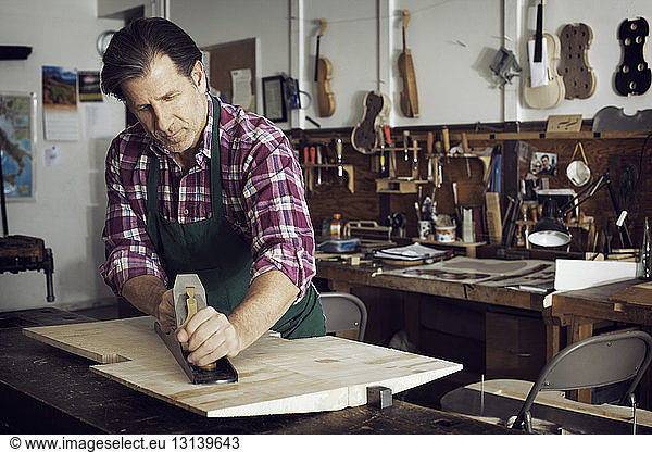 Man sawing wood while making violin in workshop