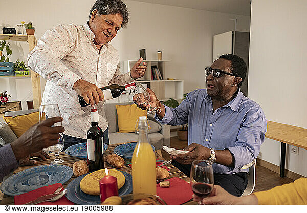 Man serving wine to senior friend sitting at dining table