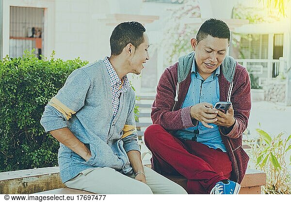 Man showing his cell phone to another guy  two guys checking their cell phones  Two young men comparing their cell phones
